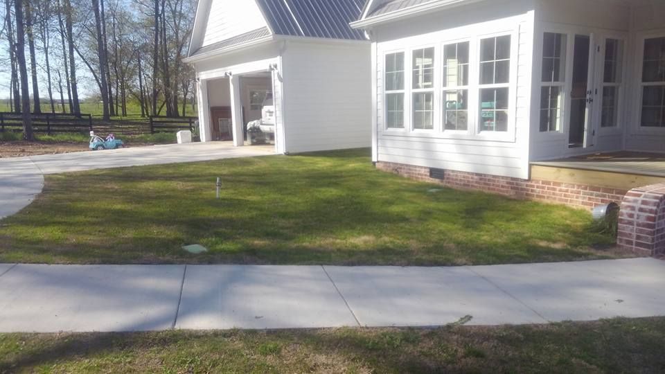 A white house with a lush green lawn and a sidewalk in front of it.