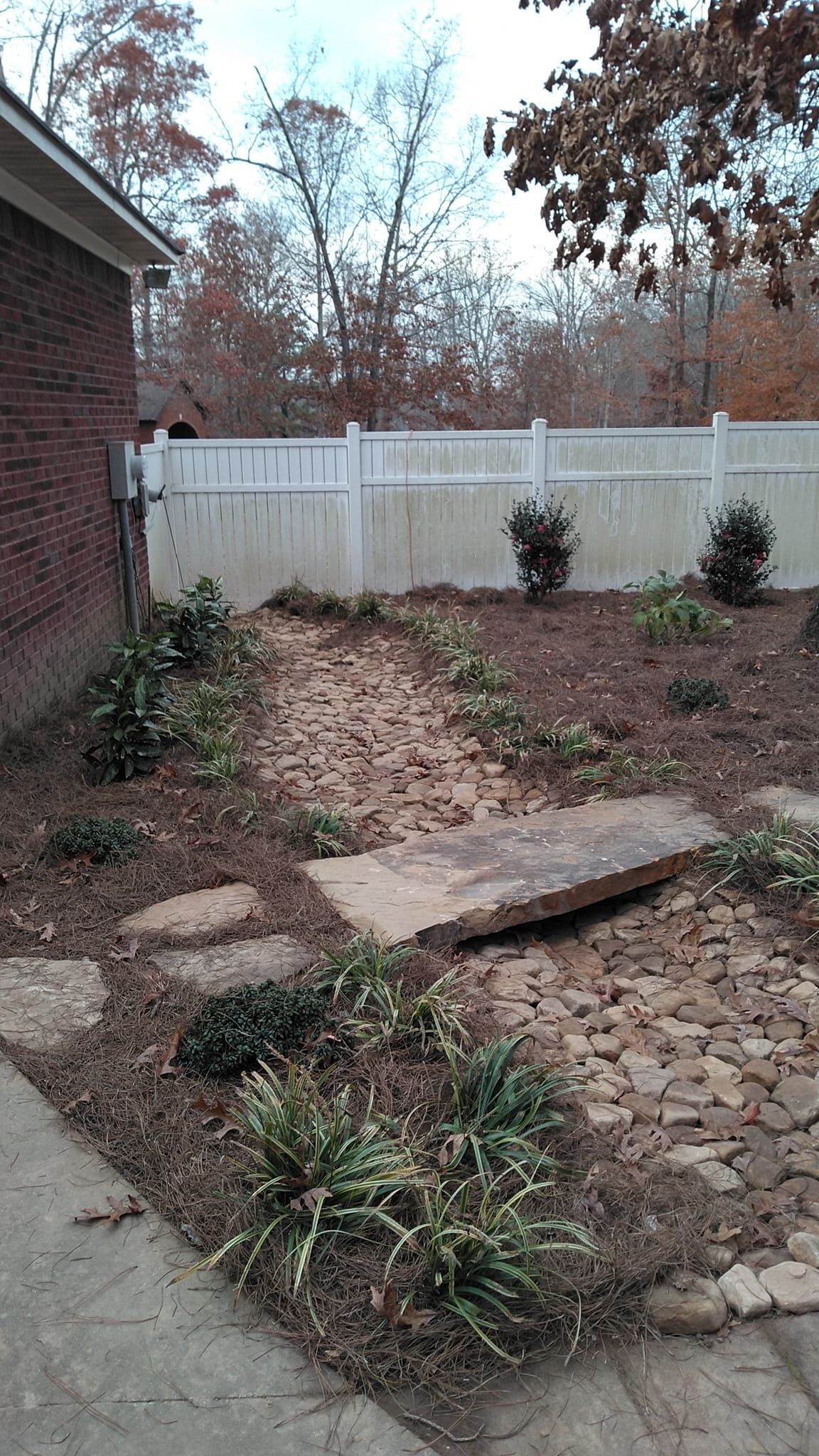 A backyard with a white fence and a stone walkway.