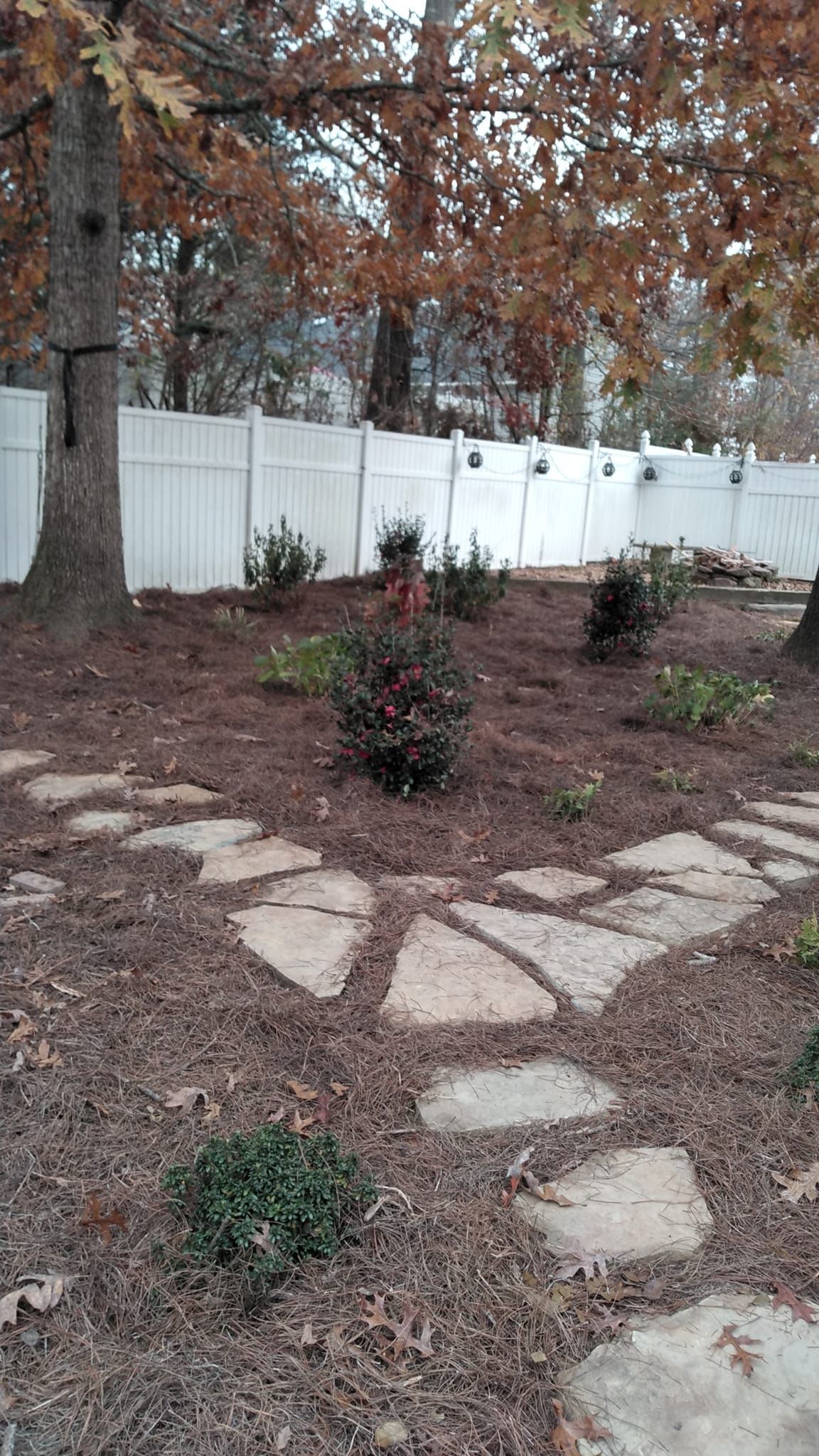 A stone walkway leading to a white fence in a backyard.