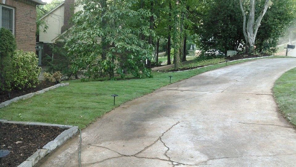 A concrete driveway leading to a house with a lush green lawn.