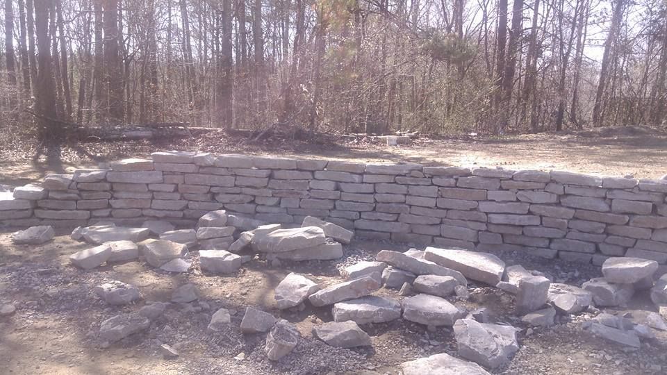 A pile of rocks is sitting in front of a brick wall in the middle of a forest.