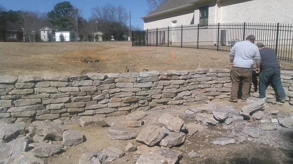 Two men are working on a stone wall in front of a house