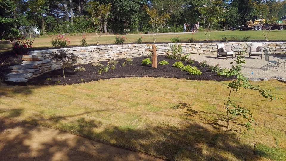 A lawn with a stone wall and a patio in the background
