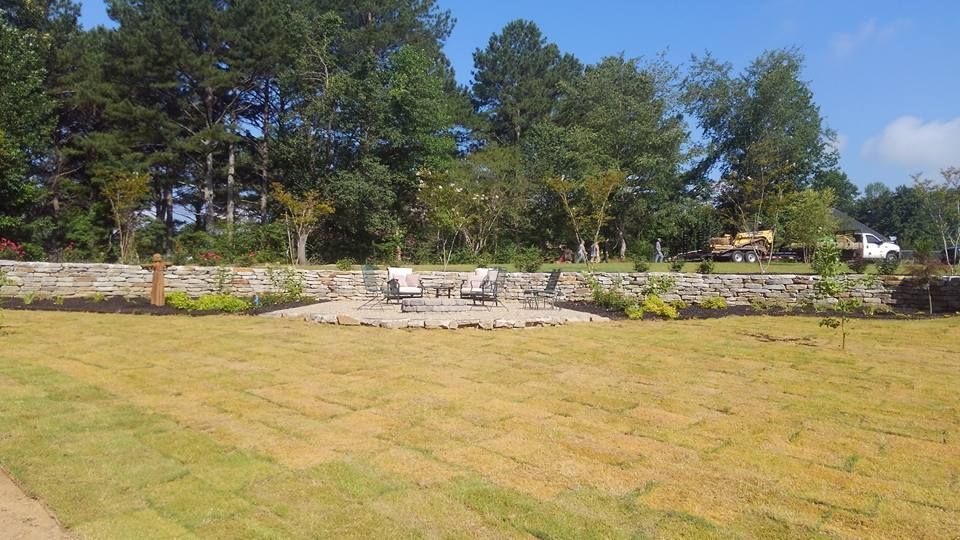 A large lawn with a stone wall and trees in the background.