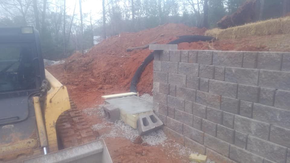 A bulldozer is driving down a dirt road next to a brick wall.
