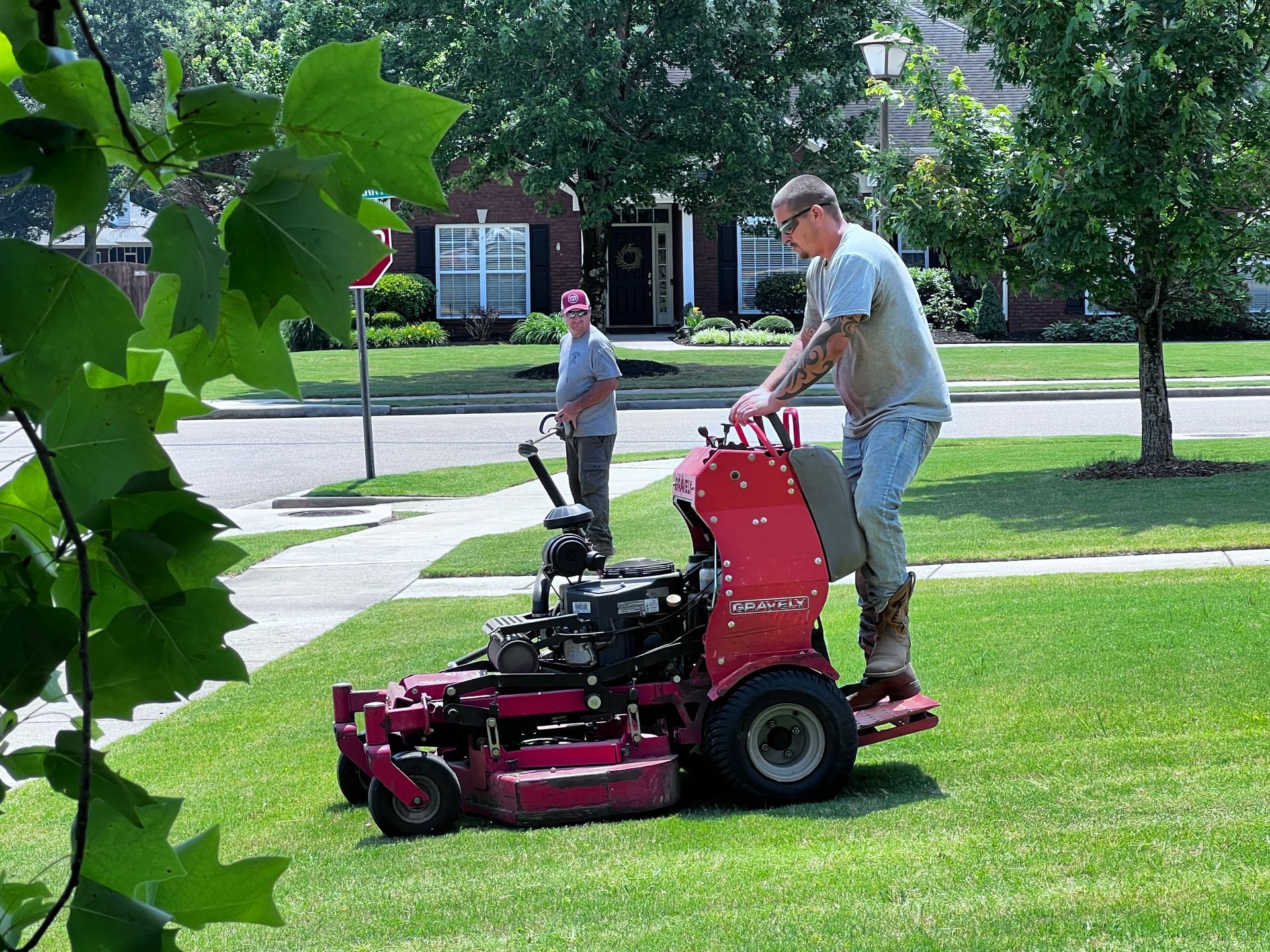 A man is riding a red lawn mower on a lush green lawn