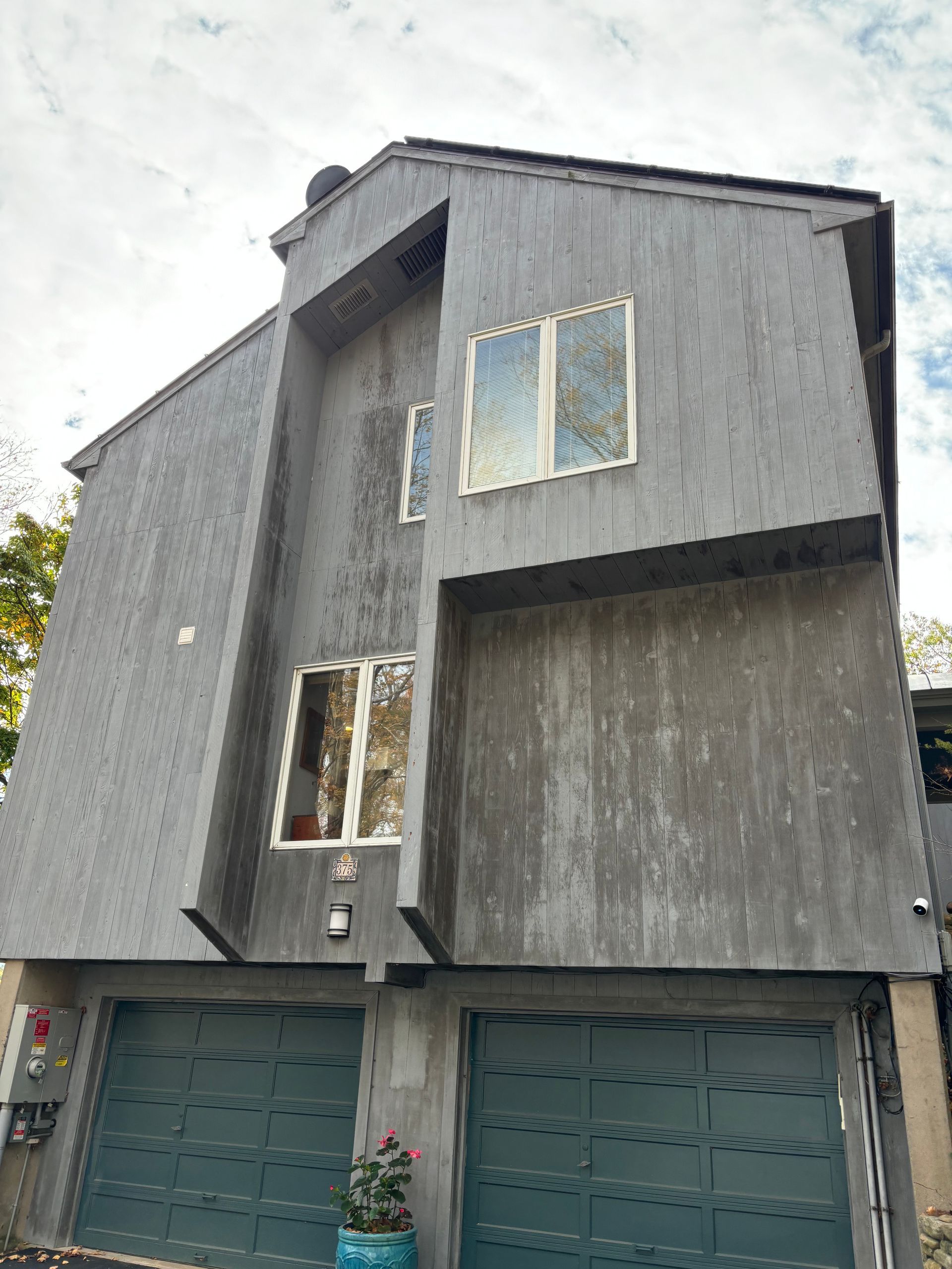 Gray townhouse with teal garage doors and white-framed windows. A potted plant sits near the garage.