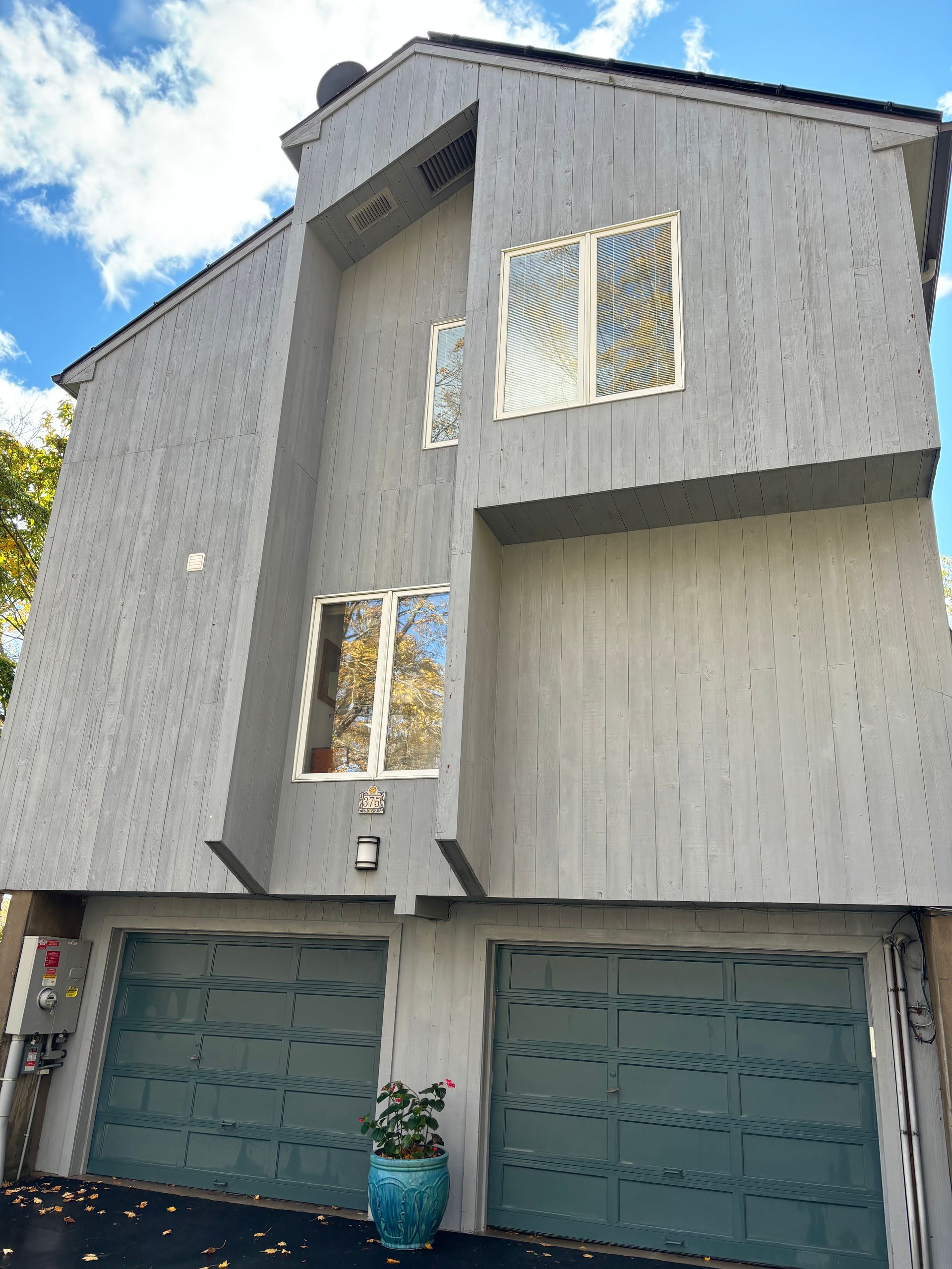 Gray two-story house with teal garage doors and a blue flower pot.