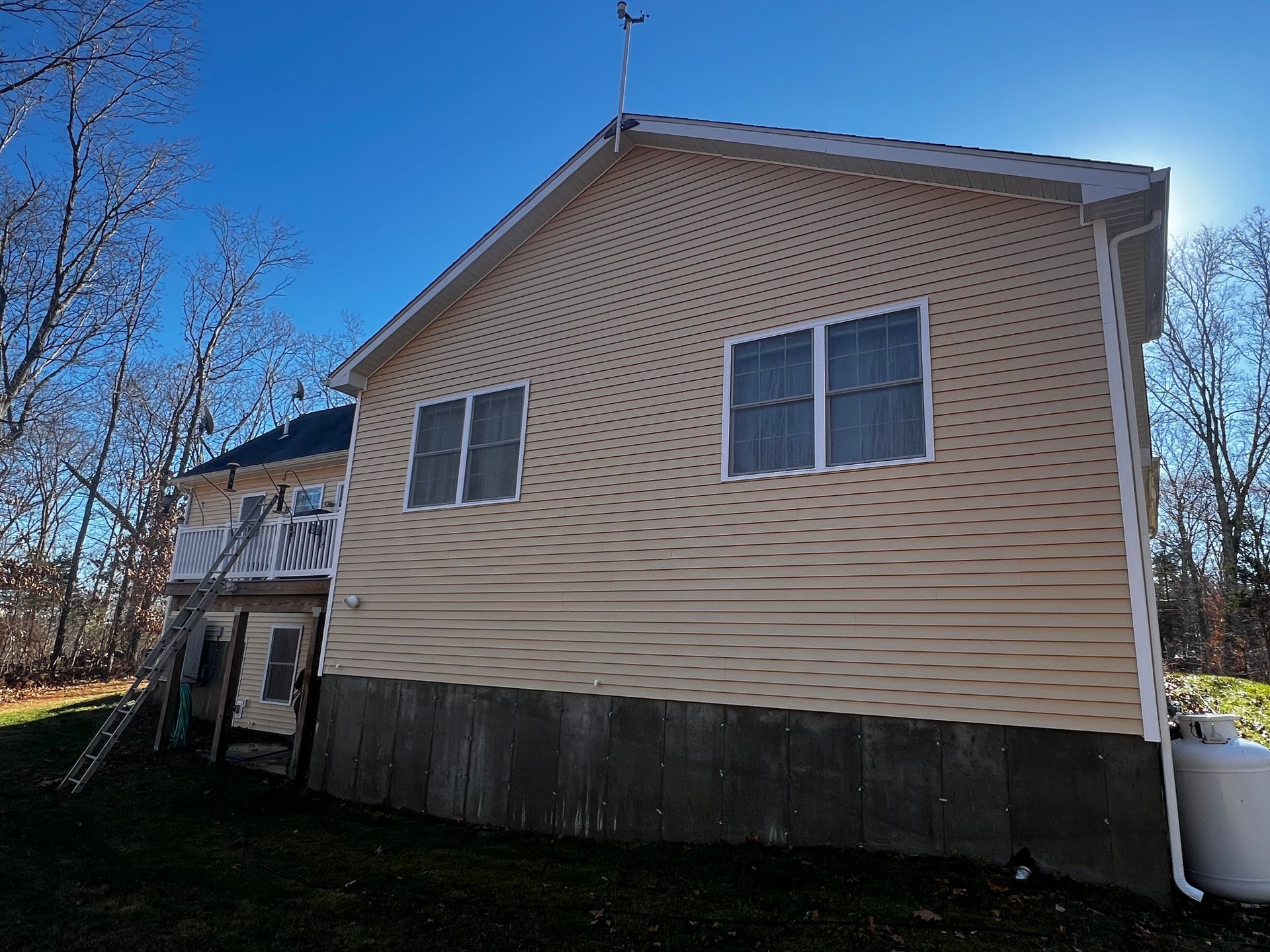 Beige house with white trim, two windows, dark lower level, against a blue sky.