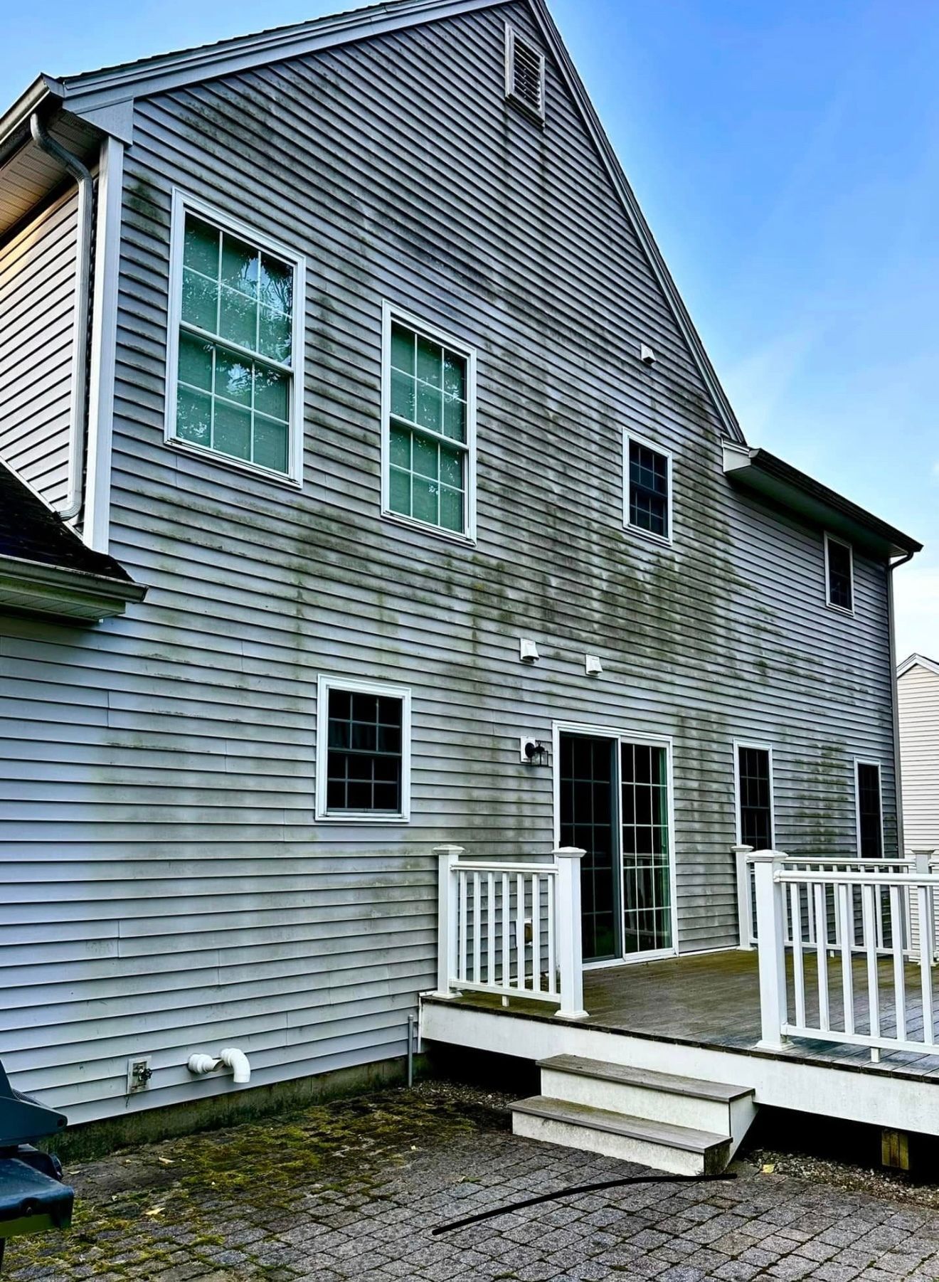 Weathered gray house with white trim, deck, and siding stained with algae.