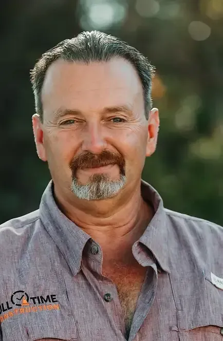 Man with brown hair and goatee, wearing a button-down shirt, smiling.