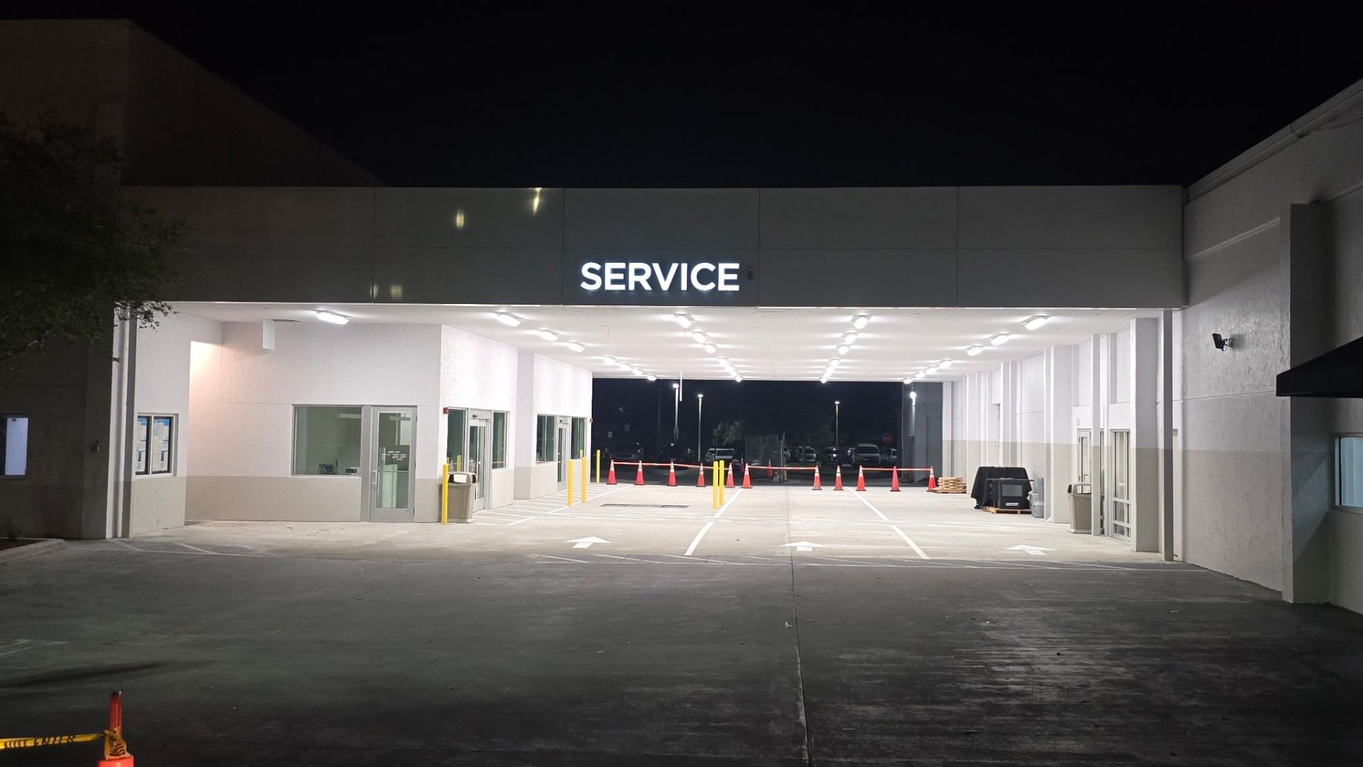 A brightly lit automotive service center bay at night, featuring a white exterior with a "SERVICE" sign above the entrance.