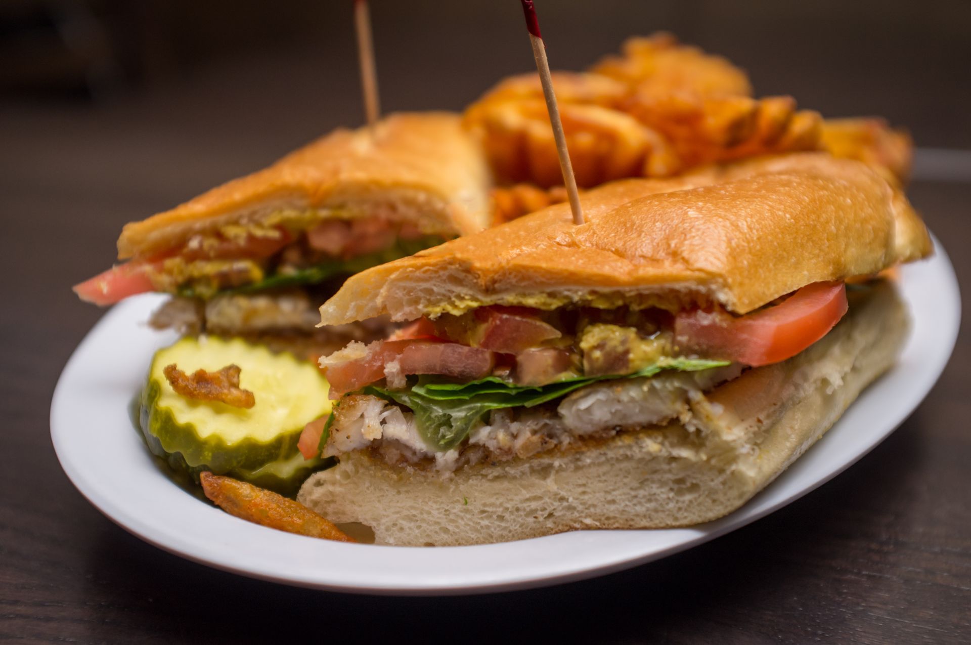 A sub sandwich with french fries on a white plate.