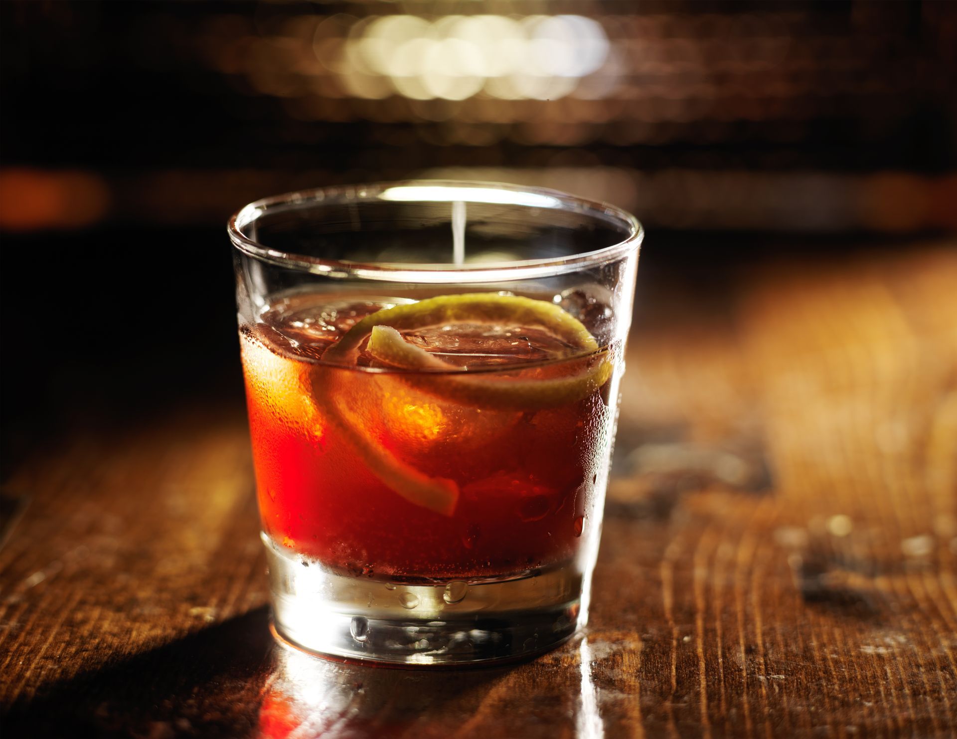 A glass of red liquid with ice and lemon slices on a wooden table.