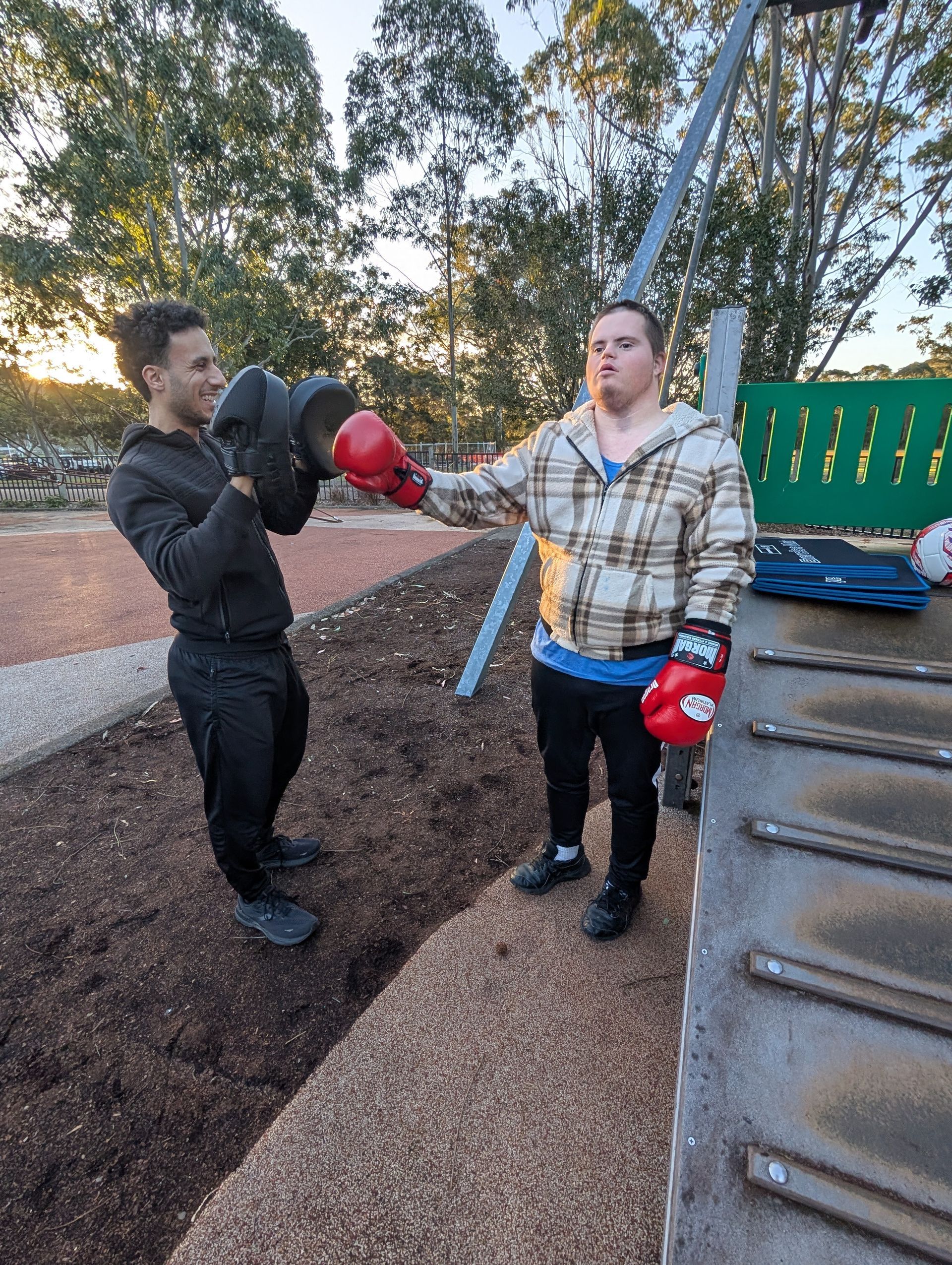 Two men boxing outdoors; one throws a punch wearing red gloves, other holds pads —True Form Fitness In Gwandalan, NSW