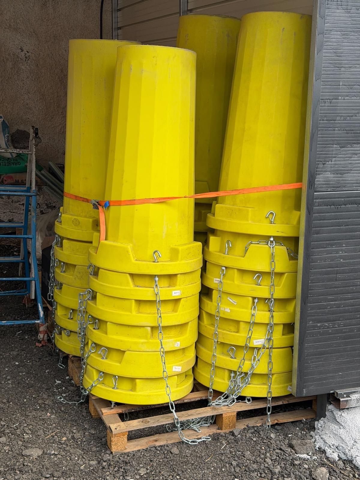 Pile di contenitori industriali in plastica giallo acceso, fissati su un pallet di legno al chiuso.