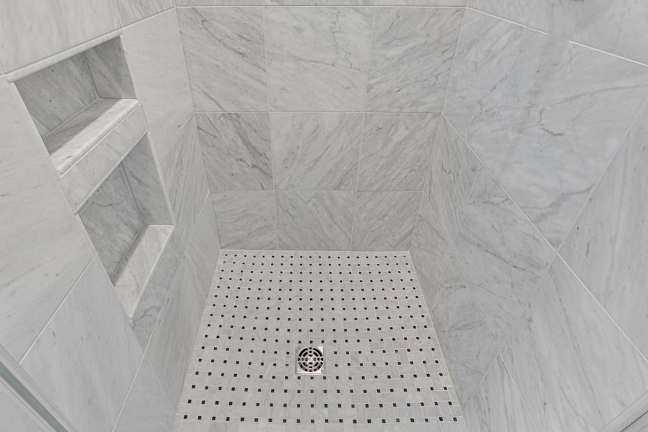 Empty tiled shower with built-in shelves and a white drain pan.