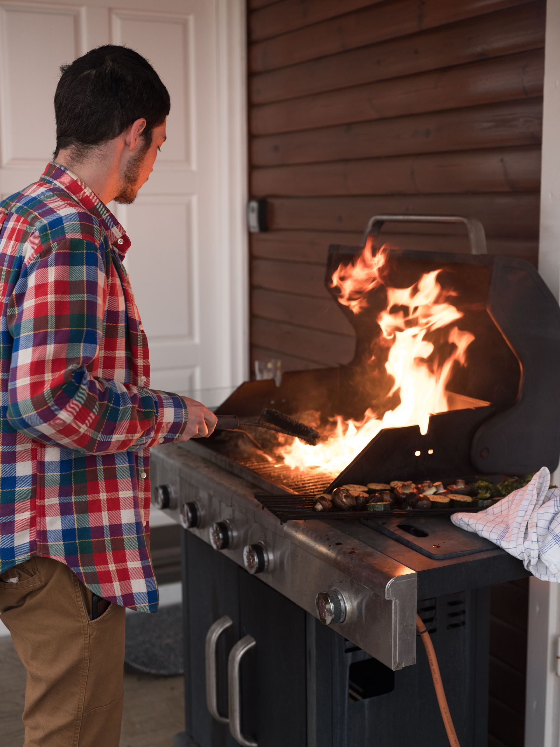 Person grilling at an outdoor barbecue with flames rising from the grill
