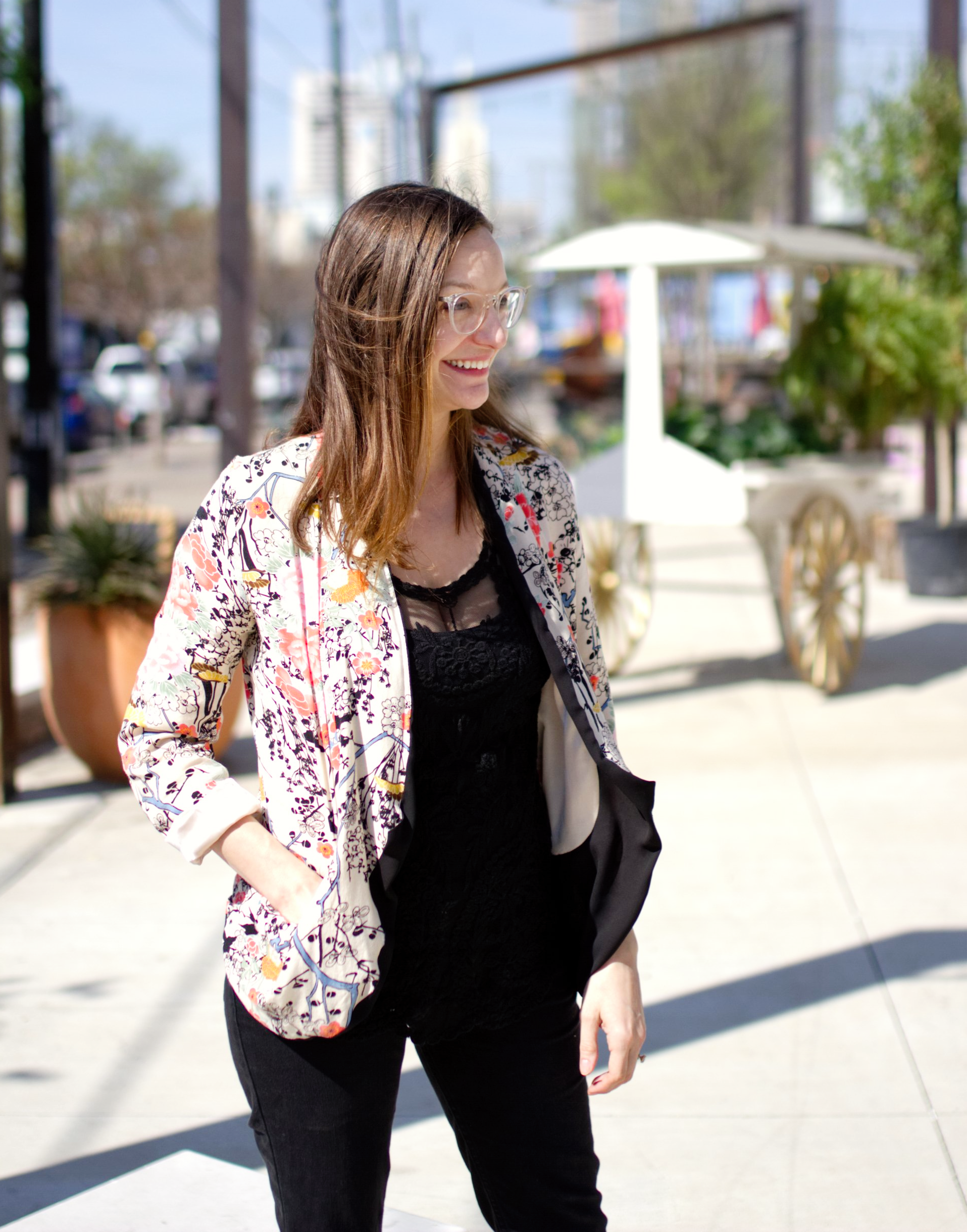 Cris Haest Woman in floral jacket and black outfit smiles outdoors, hands in pockets.