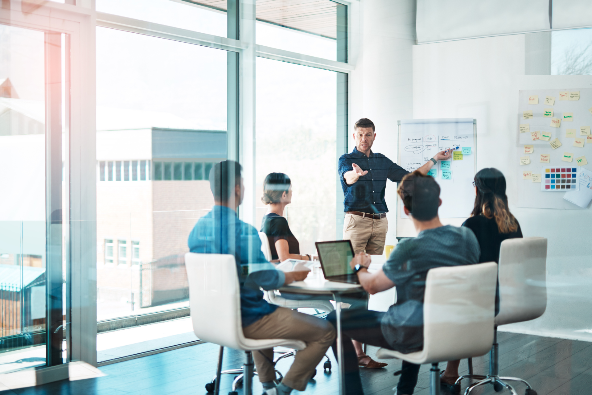 marketing growth Office meeting: Man presenting to colleagues at whiteboard near a window.