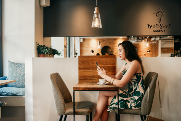 Woman in a cafe looking at phone. She sits at a wooden table with a coffee cup. White and dark gray interior.