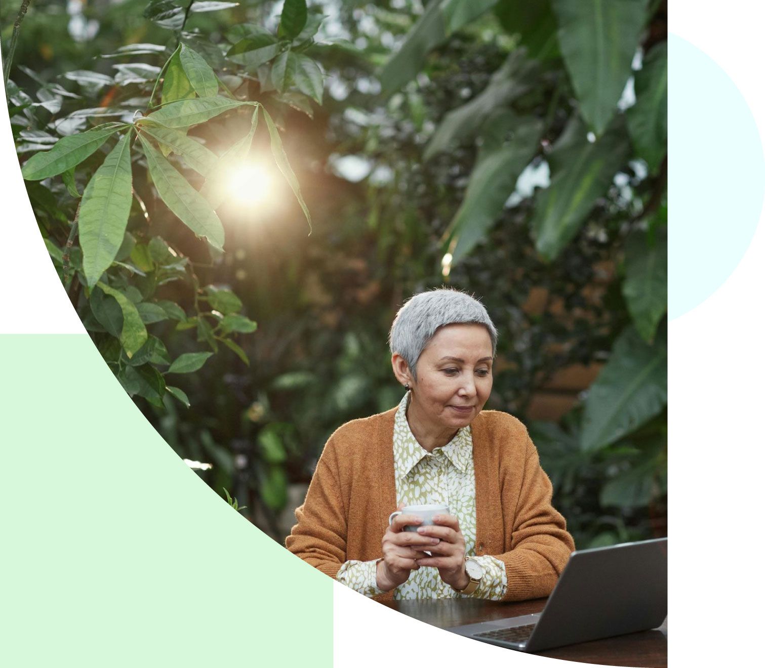 An elderly woman is sitting at a table with a laptop and a cup of coffee.