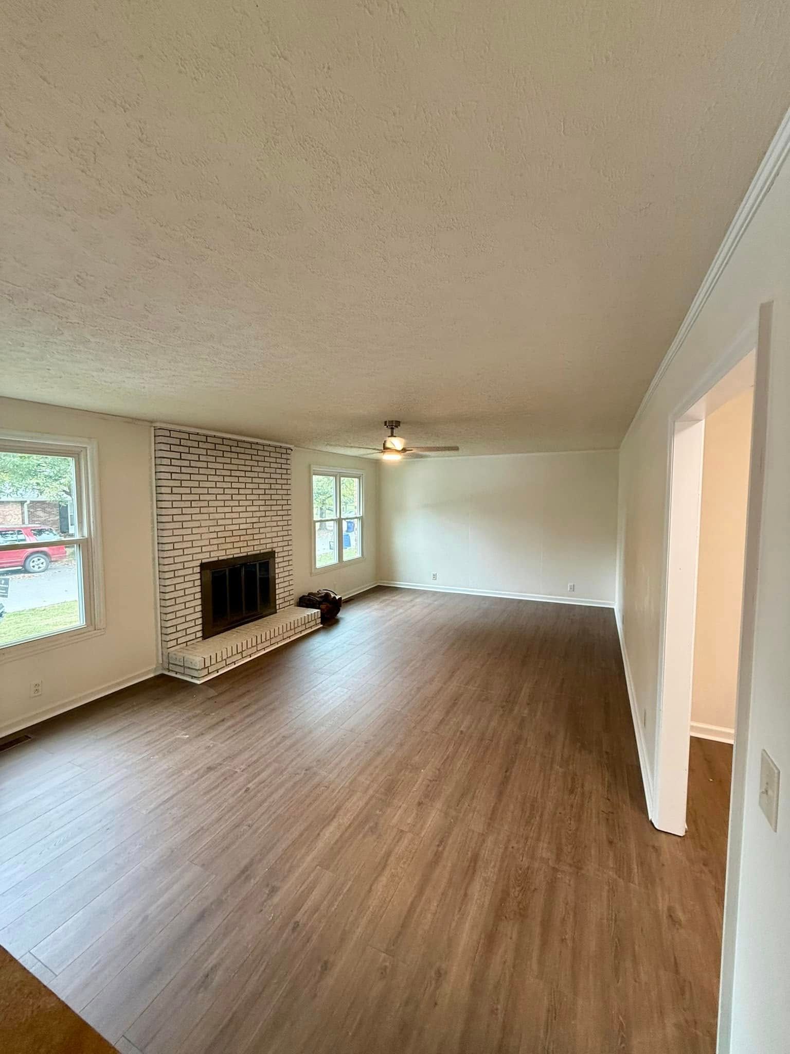 A living room with hardwood floors , a fireplace and a ceiling fan.