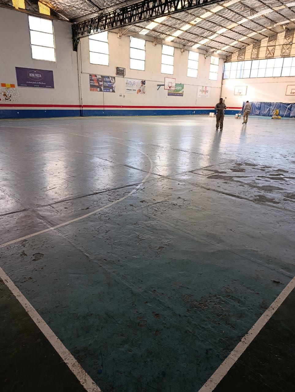 Gimnasio cubierto con suelo brillante, pancartas en las paredes y una persona de pie cerca de la pared del fondo.
