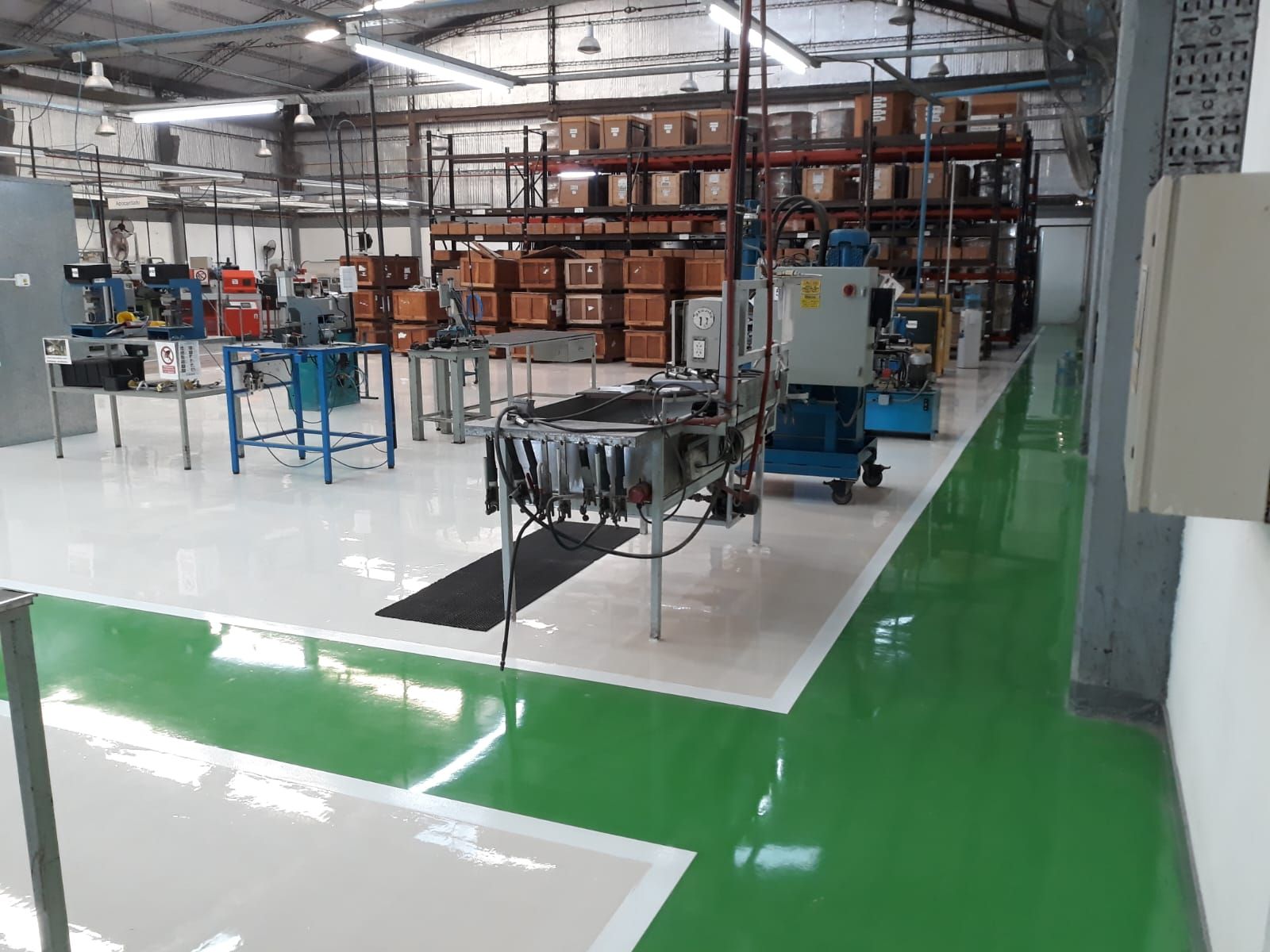 Almacén industrial con suelo, estanterías y maquinaria de color verde y blanco brillante, iluminado desde luces cenitales intensas.