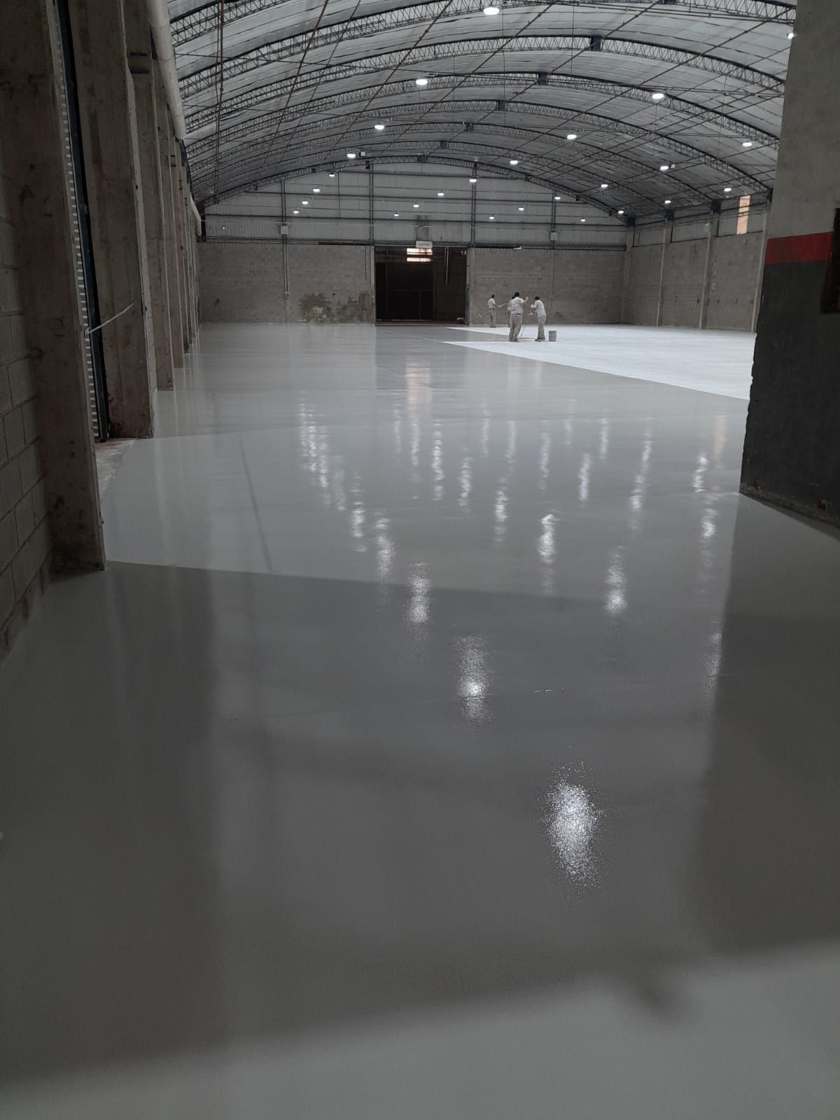 Interior de un almacén vacío con suelo blanco brillante y techo metálico arqueado.