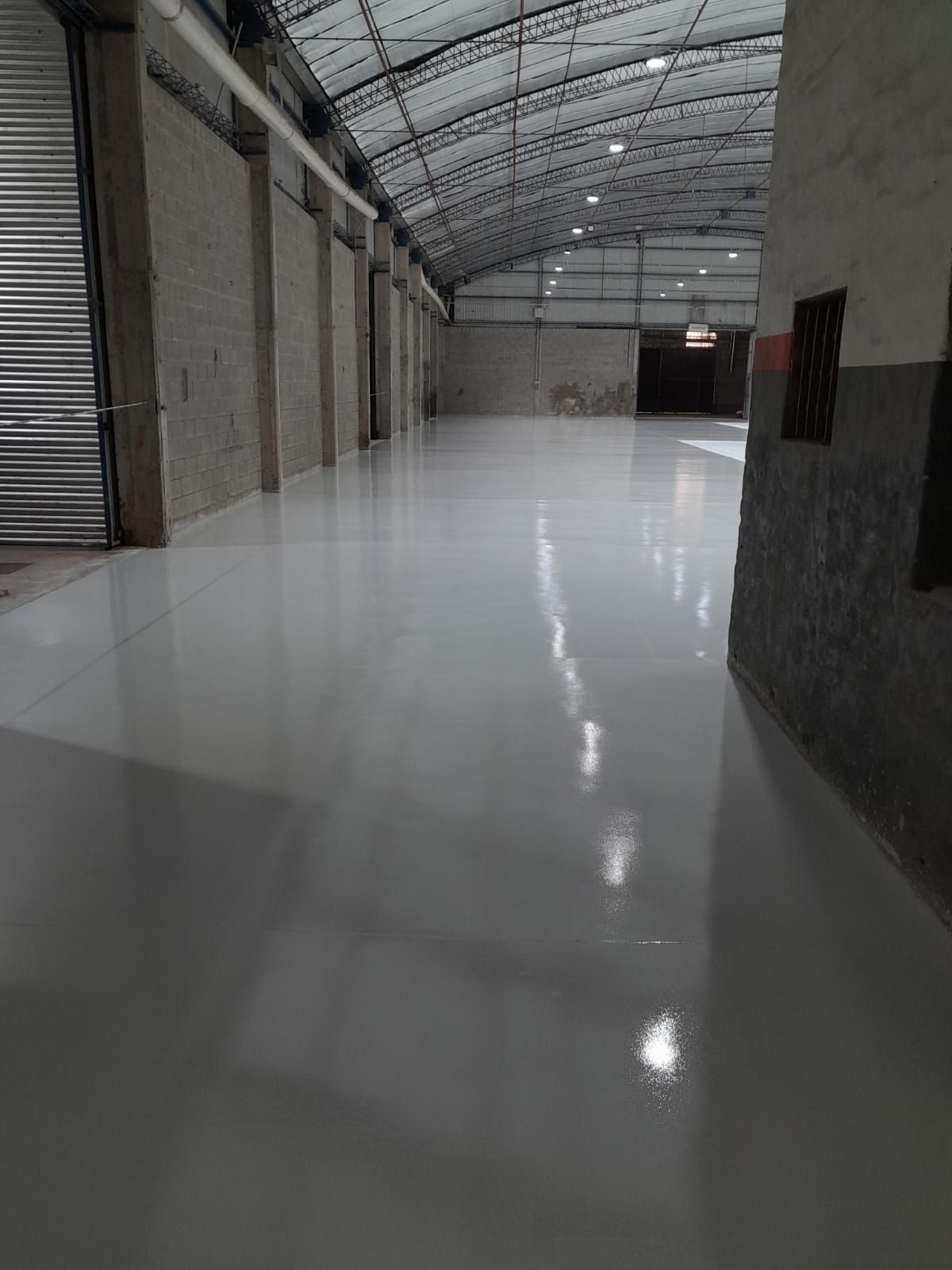 Interior vacío de un almacén industrial con suelo blanco brillante y techo metálico arqueado.