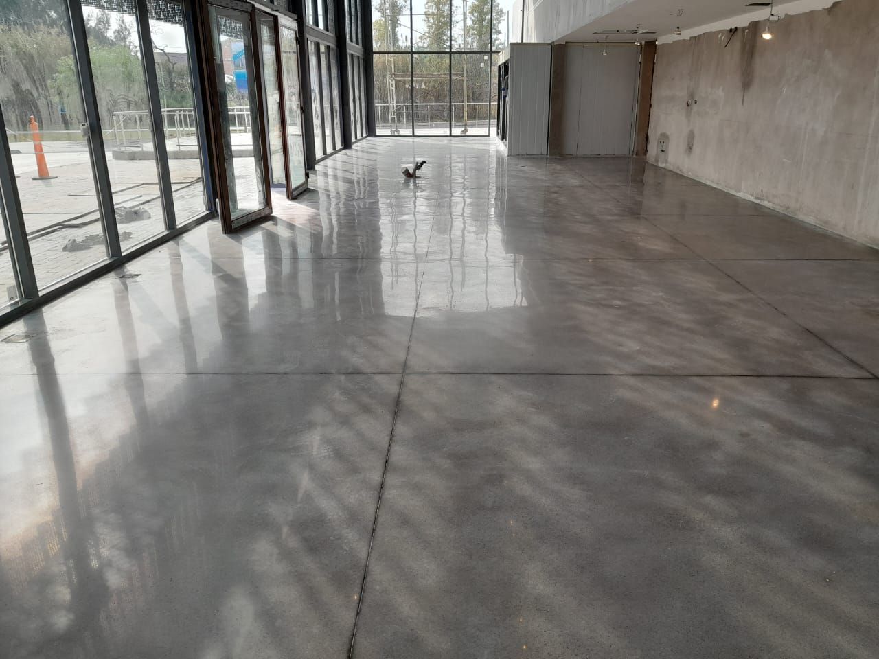 Vestíbulo moderno y vacío con suelo de hormigón brillante y ventanales que van del suelo al techo y reflejan la luz.