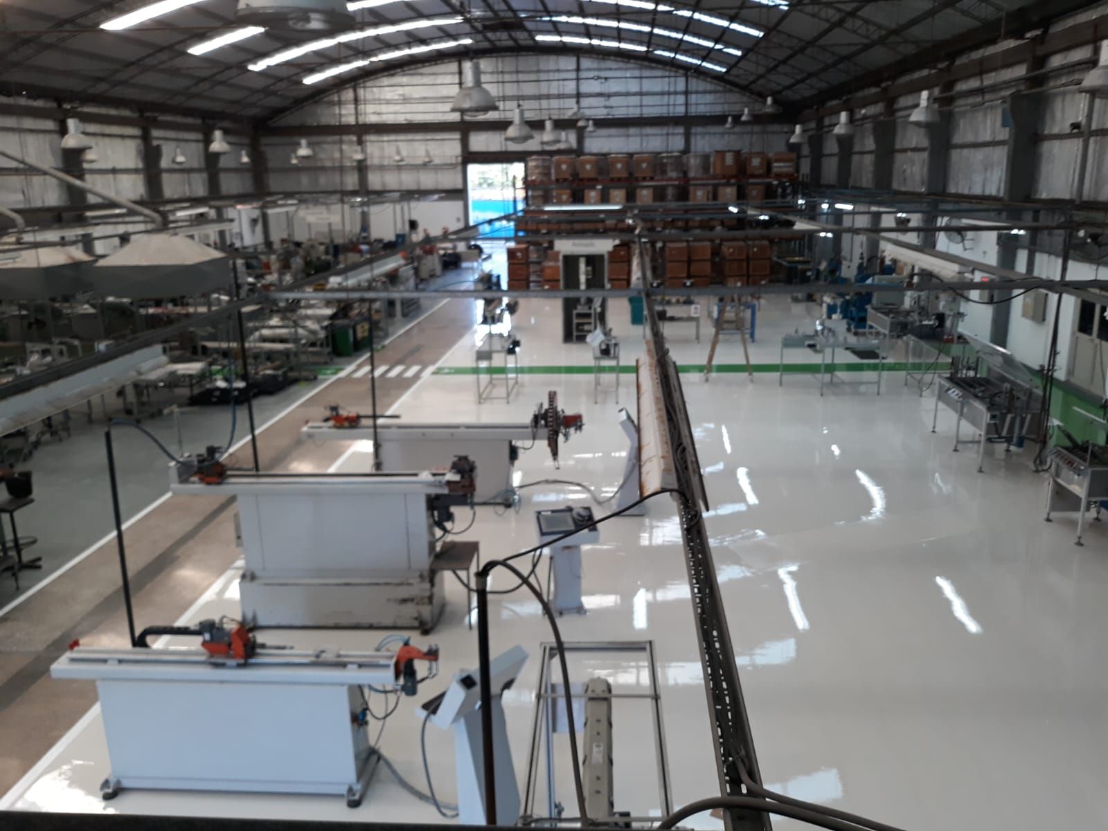 Interior de una gran nave industrial con máquinas, mesas de trabajo y un suelo blanco brillante.