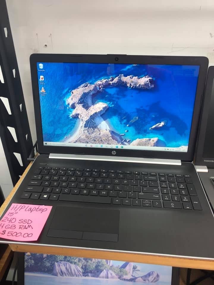 Black HP laptop on a desk with a blue ocean wallpaper and pink sticky notes on the left corner