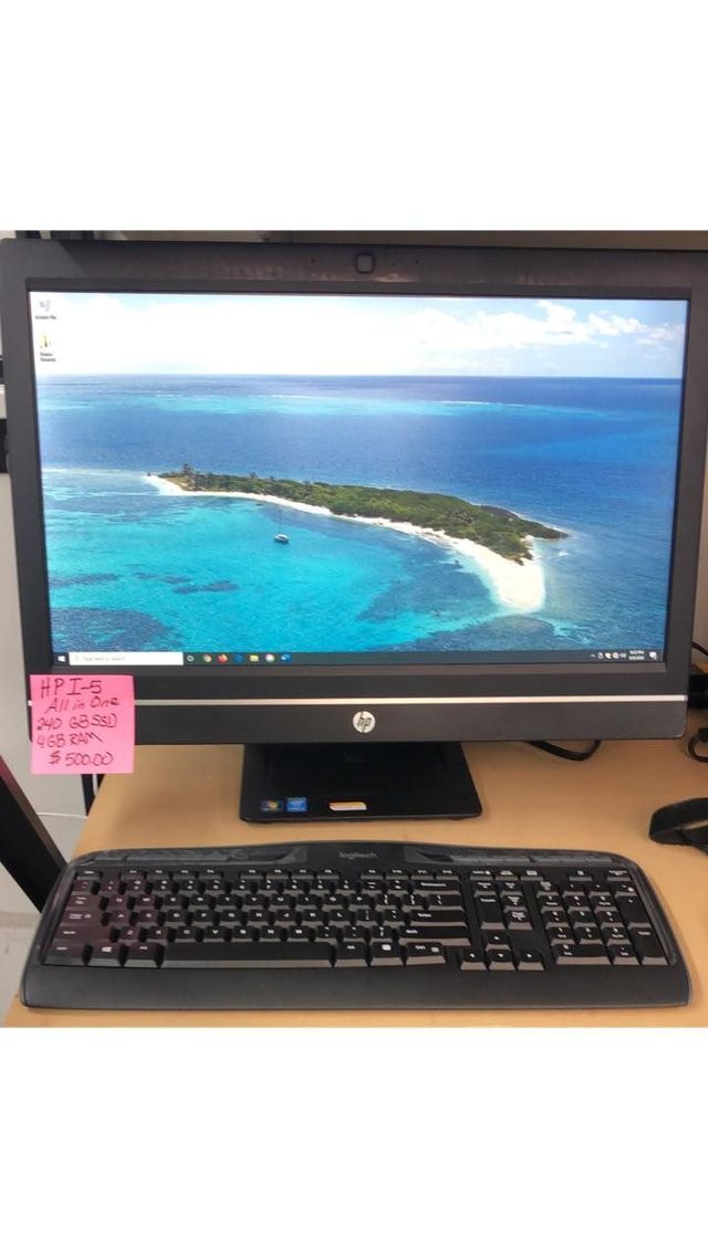 Desktop monitor displaying an ocean island wallpaper, with keyboard and sticky note on a desk.