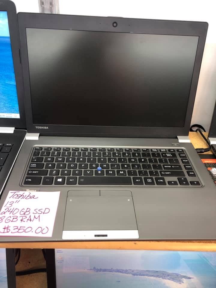 Black HP laptop on a desk with a handwritten price sign beside it and a charging cable plugged in