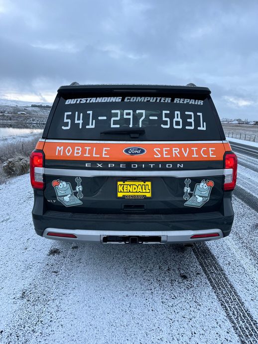 Black pickup truck with “Mobile Service” and phone number on snowy road, rear view