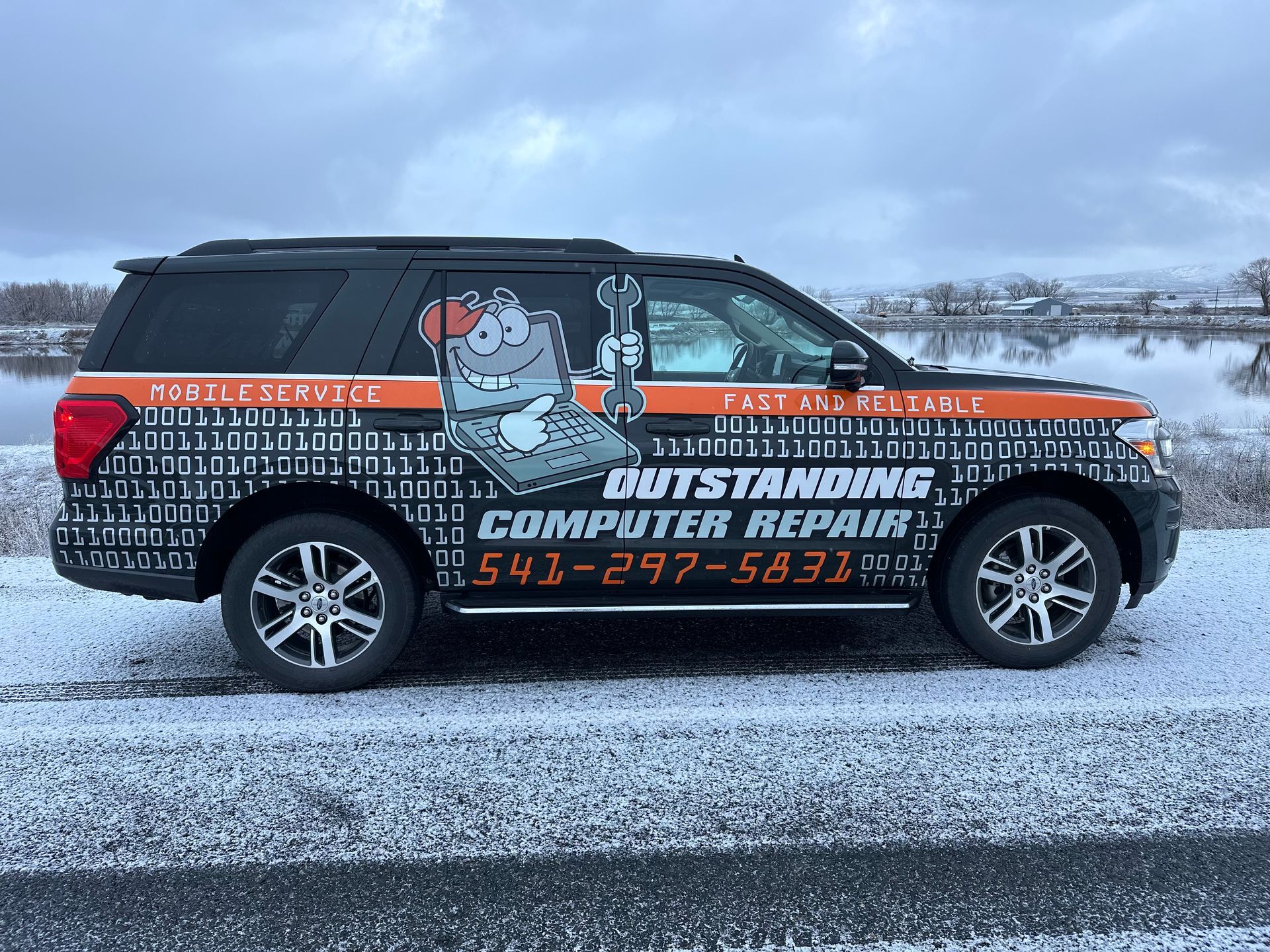 Branded black van with orange stripes and a cartoon mascot parked on snowy roadside, advertising computer repair.