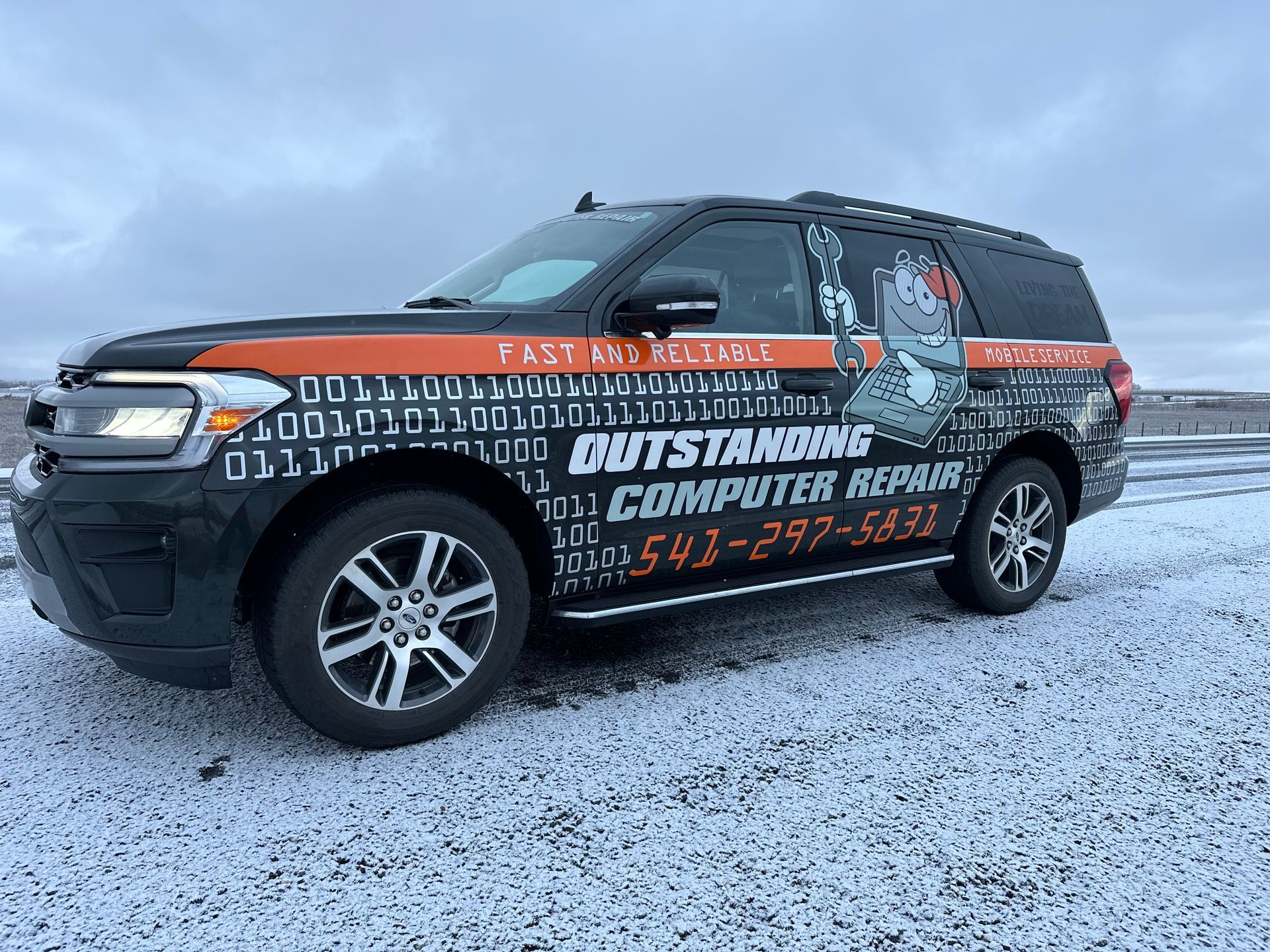 Wrapped black SUV on a snowy roadside with “Outstanding Computer Repair” advertising.