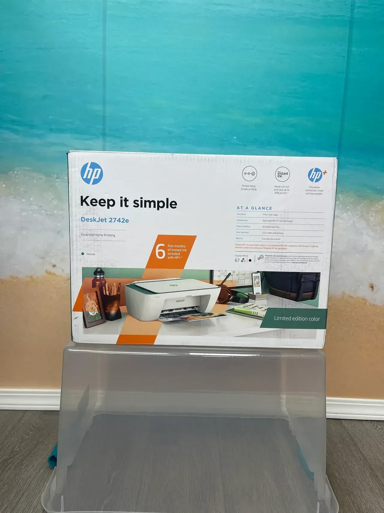 HP printer box displayed on a clear stand against a teal wall with a white baseboard.