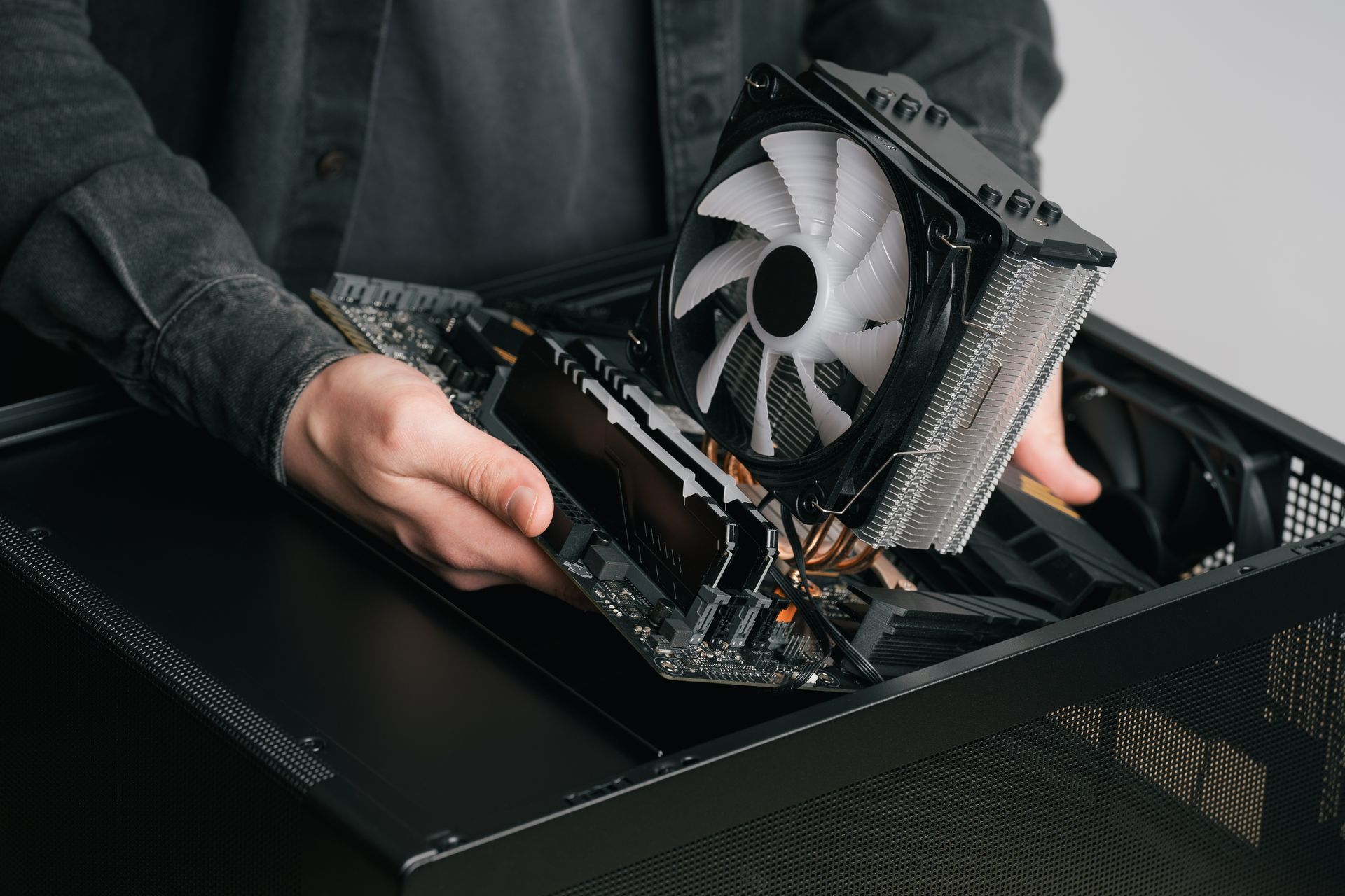 Hands installing a graphics card into a desktop computer case on a black desk