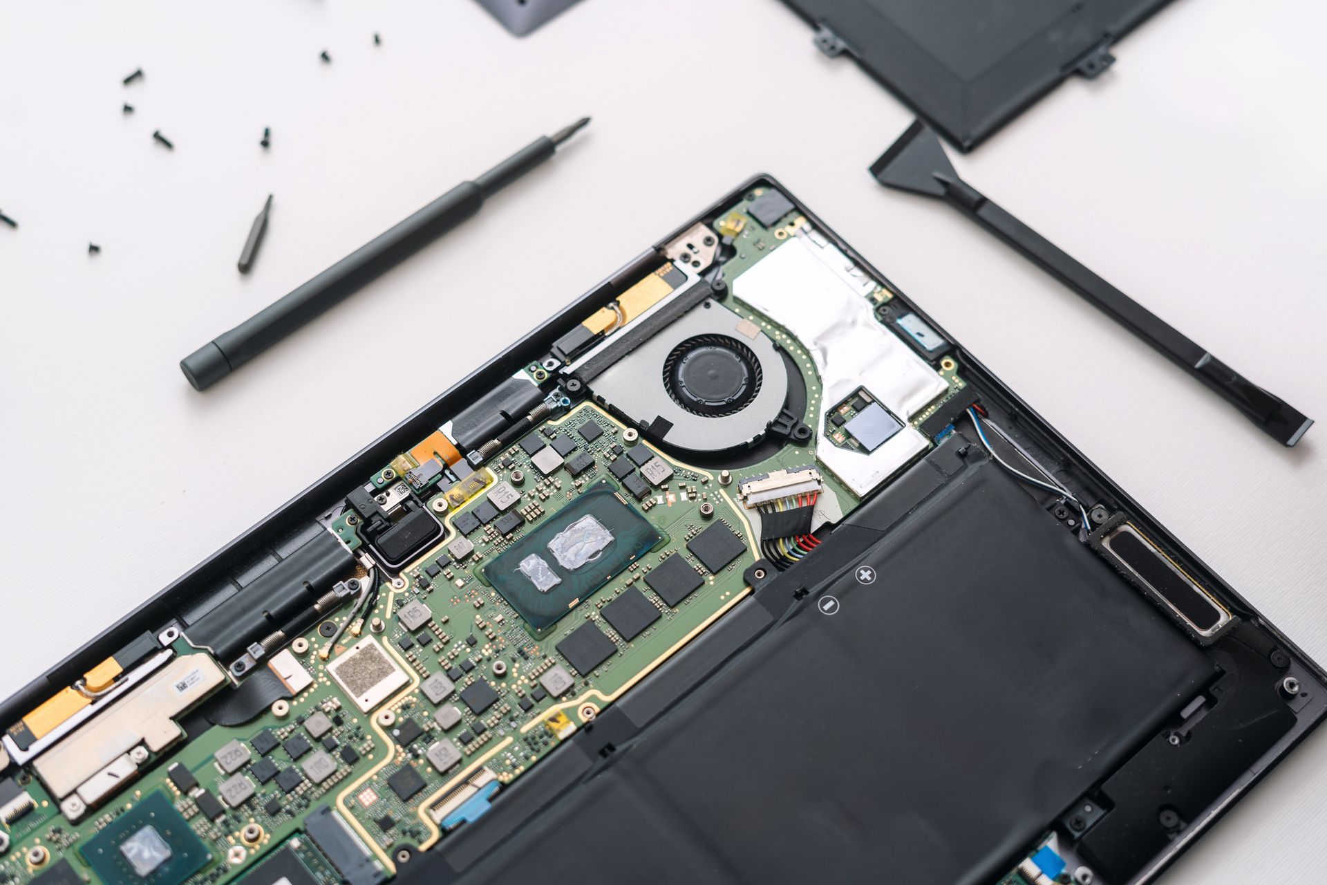 Open laptop with exposed internal components and scattered tools on a white surface