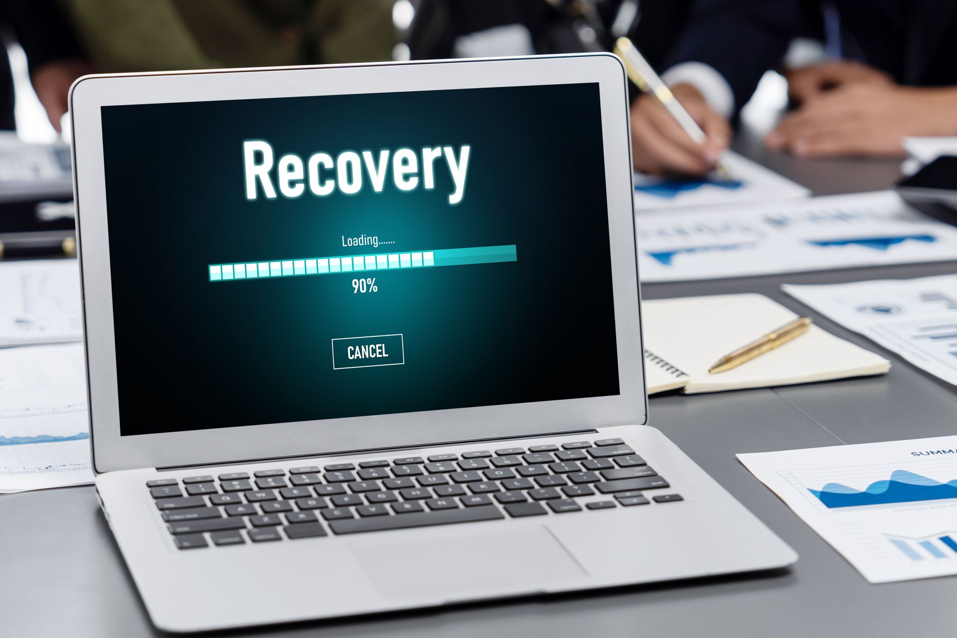 Laptop on a desk showing “Recovery” on the screen, with paperwork and charts in the background