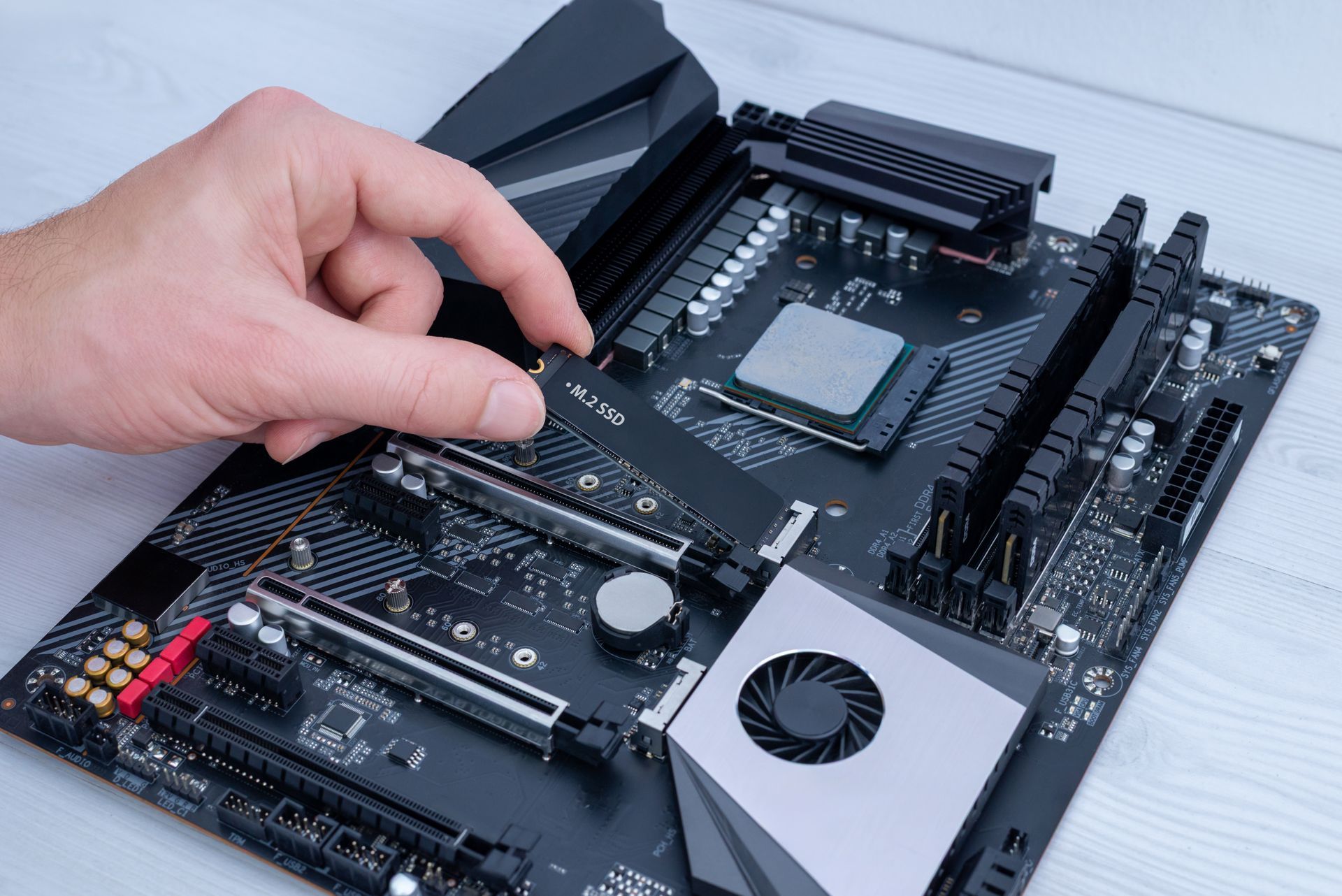 Hand placing a circuit board into a black computer motherboard on a white surface