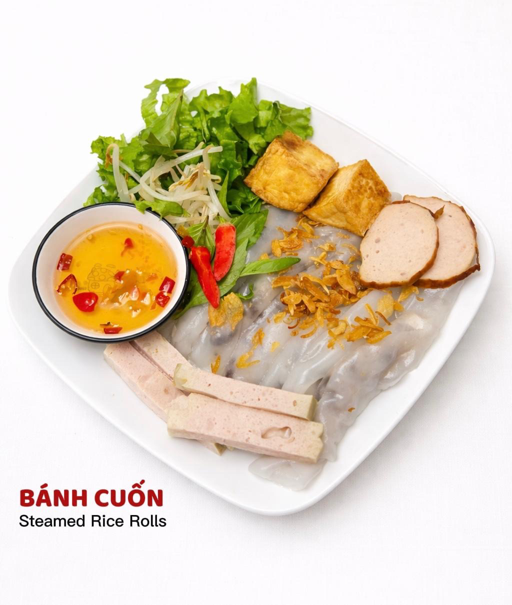 A plate of Bánh Cuốn (steamed rice rolls) with fried tofu, sliced sausage, fresh greens, and a bowl of dipping sauce.