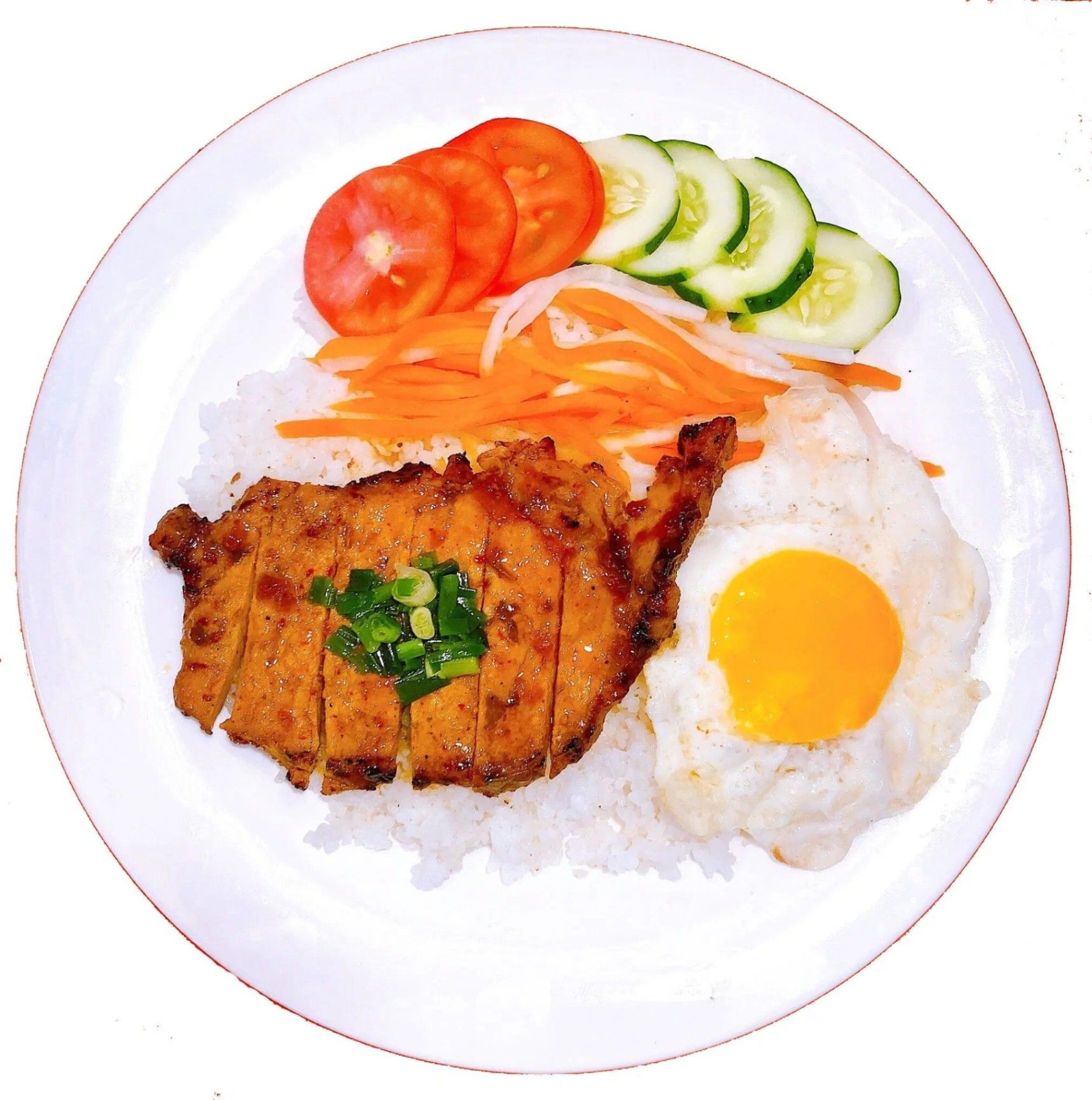 A plate of rice topped with a grilled pork chop, a fried egg, shredded carrots, tomato slices, and cucumber slices.