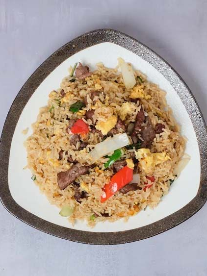 Plate of rice with meat and red pepper on a white, triangular dish