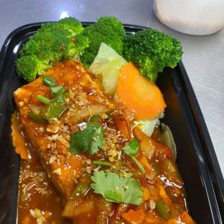 Glossy sauced entrée with broccoli and cilantro garnish on a black takeout container
