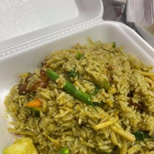 Takeout container of greenish fried rice with vegetables and meat chunks