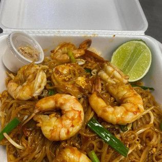 Shrimp pad thai in a takeout container with lime wedge and chili sauce cup